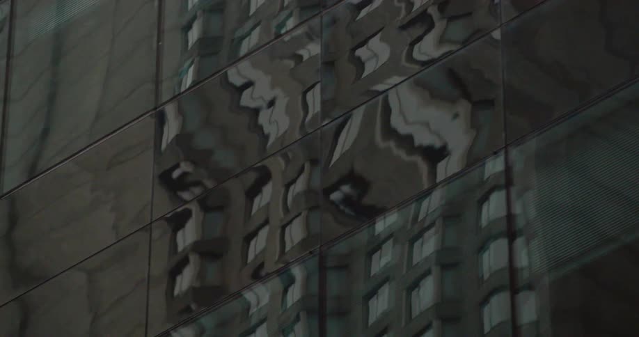 The distorted reflection of a high rise building in shown in mirrored windows of another building