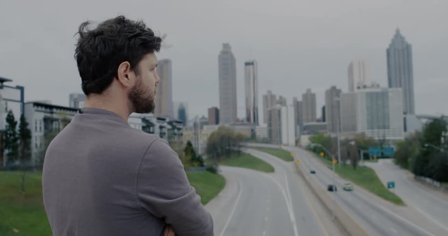 A man is standing by a downtown city while cars are driving
