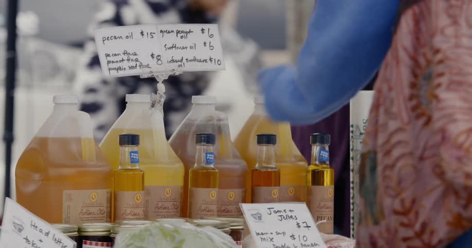 A woman with a pink skirt and blue sweater pointing at bottles of oil