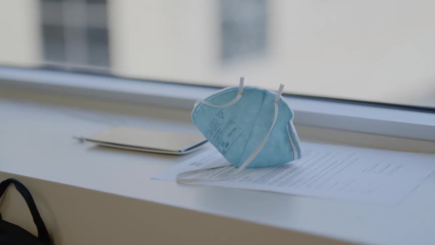 A medical face mask with elastic straps sits atop a paper on a window sill