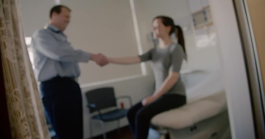 A man shaking the hand of a woman sitting on an examination table
