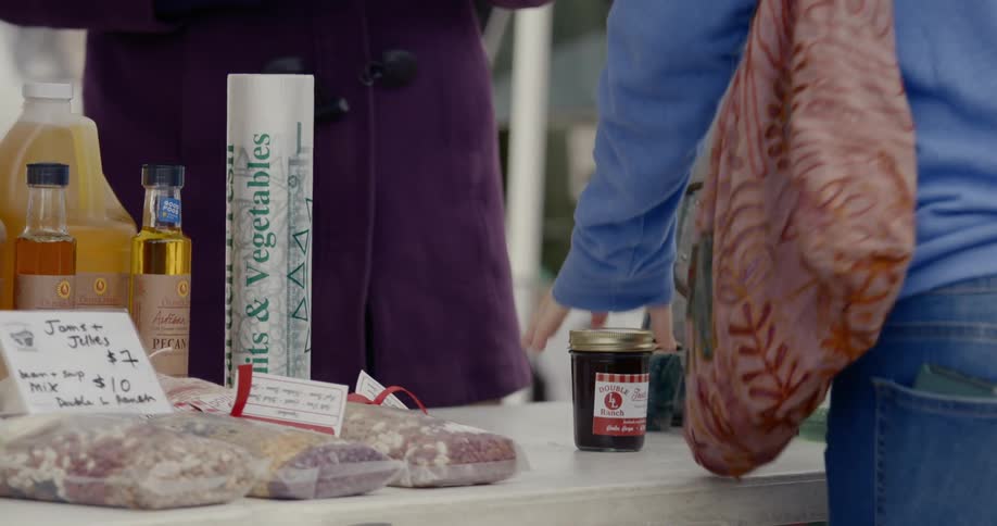 A woman reaches to a table for a jar of something at a market