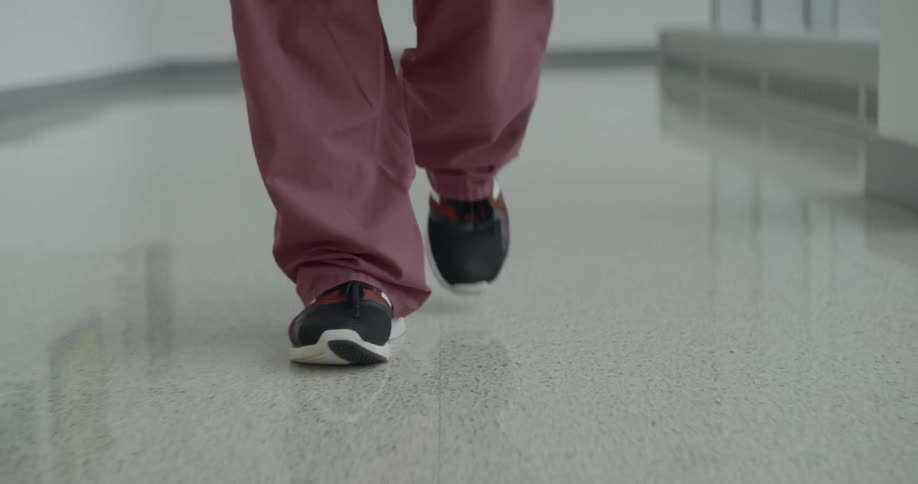 A person walks down the hallway in red scrubs and athletic shoes