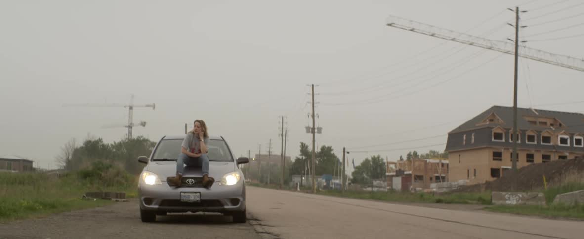 Woman sitting on a hood of car on the roadside uses smartphone