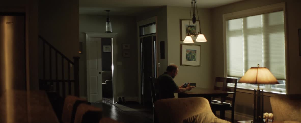 A man sitting at a dining table in his home holds and shakes a closed box