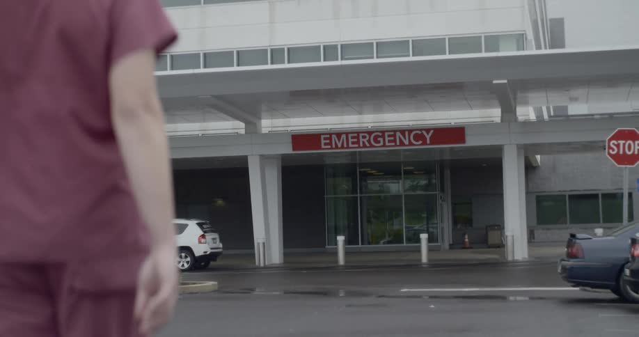A medical professional in red scrubs approaches the emergency room entrance
