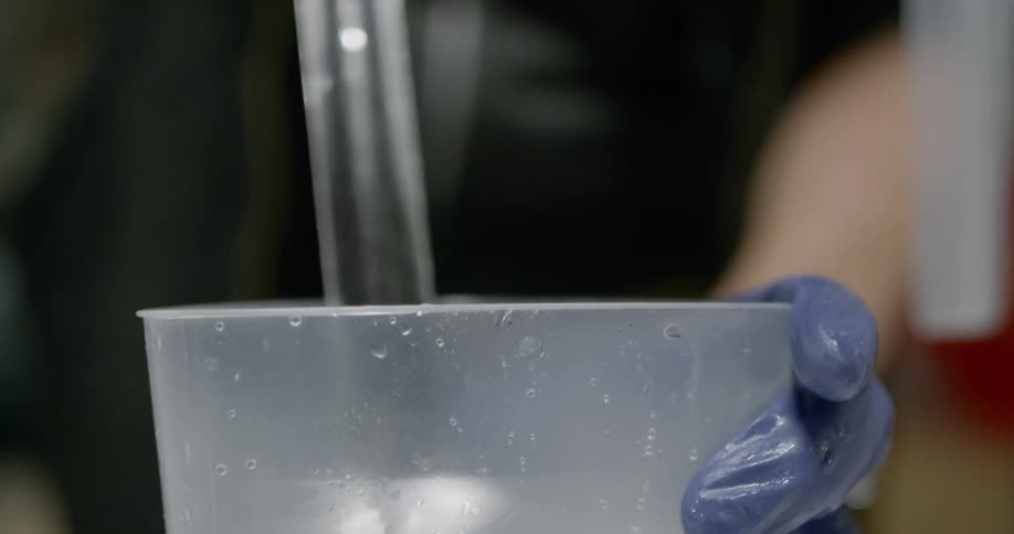 A person using a large spoon to mix a clear liquid in a plastic container