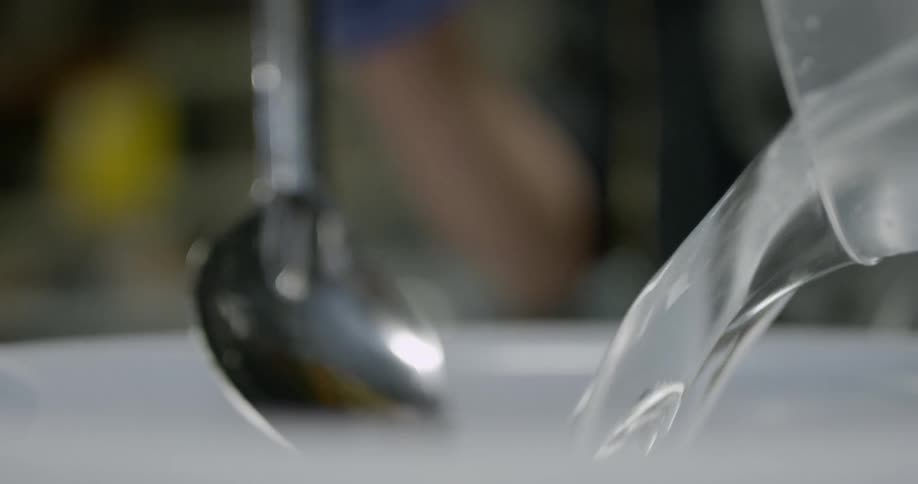 A person pouring water into a white basin while holding a silver spoon