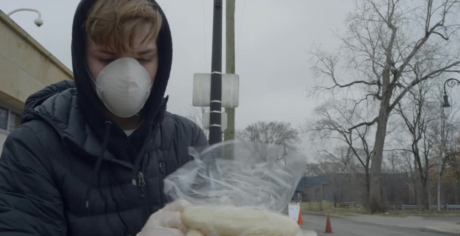 A man wearing a face mask and gloves taking groceries from a shopping cart in a parking lot