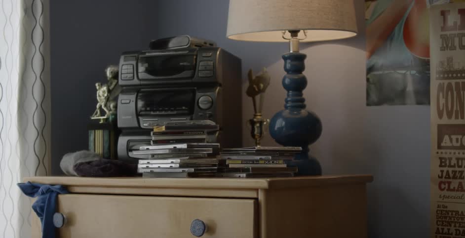 A bedroom wall is covered with posters and a dresser is stacked with cds and stereo and trophies