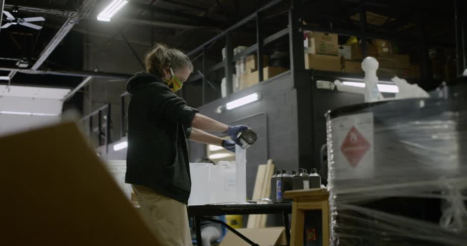 A woman pours liquid into a graduated cylinder in a warehouse