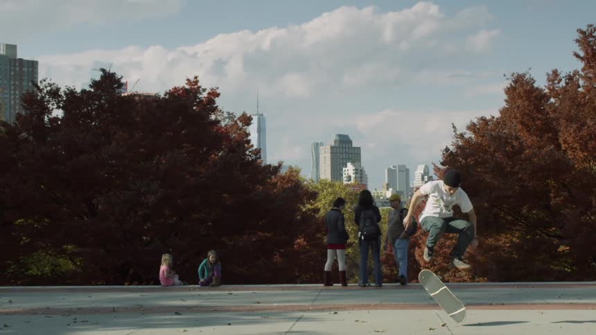 A man in a white shirt flips his skateboard