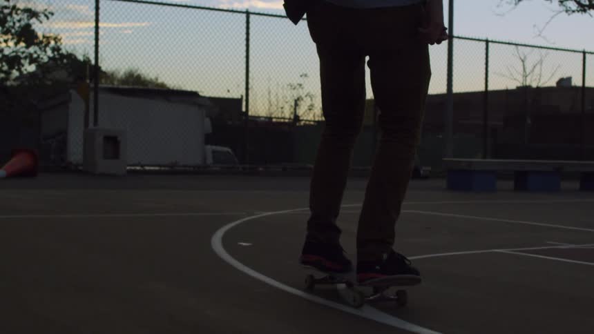 A man skateboards on a basketball court at dusk