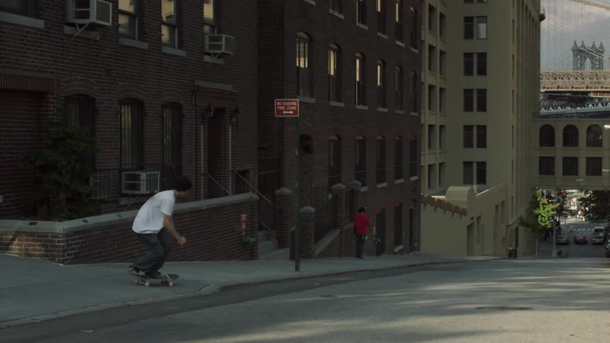 A man in a white shirt skateboards down a hill
