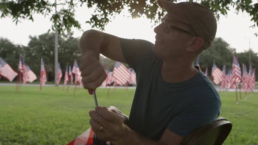 A man screwing something on a flag pole as numerous flags flap in the breeze behind him