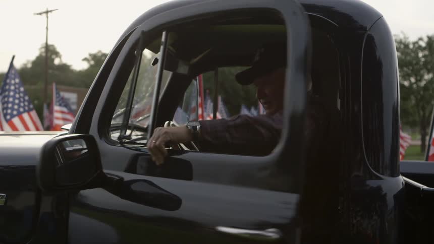 A man sits at the wheel of a pickup truck and closes the door