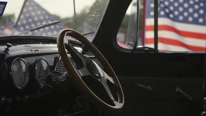 A vintage truck is parked with american flags waving behind it