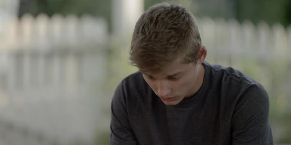 A young man shaking his head while sitting in a yard surrounded by a white fence