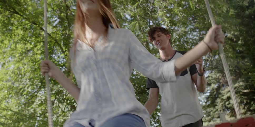 A young man pushes a young woman on a swing