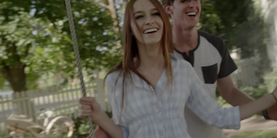 A young man pushes a young woman on a swing