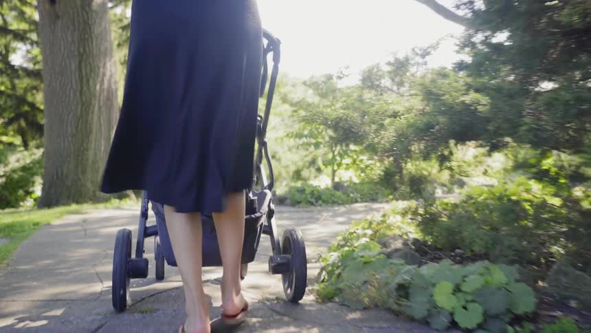 Woman wearing a blue dress pushes a baby stroller in the public park