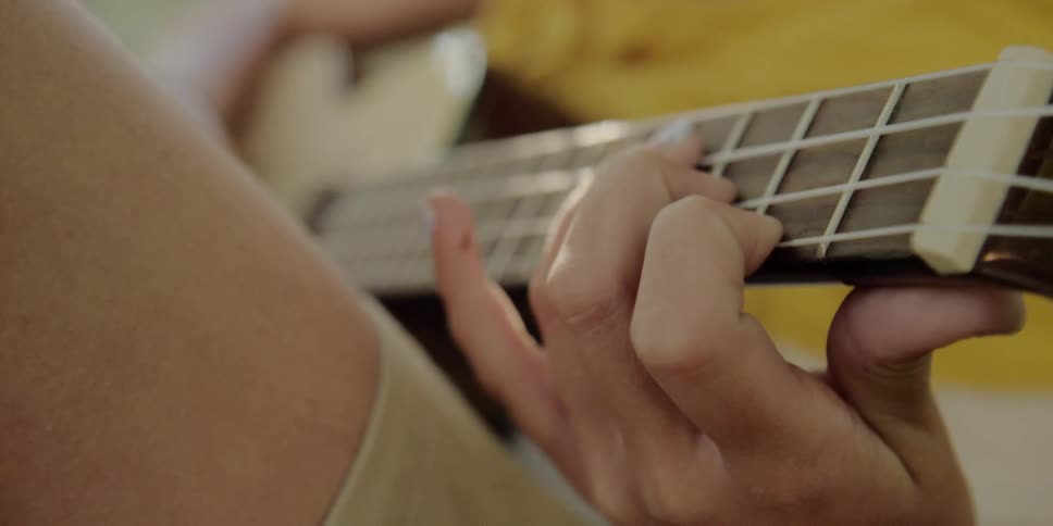 A female is sitting while playing chords on an acoustic guitar