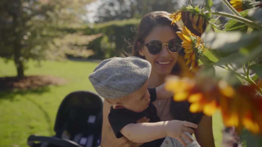 A young woman holds a baby boy up towards a sunflower so that he can touch it