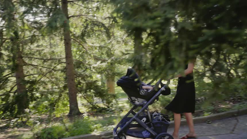 Woman wearing a blue dress pushes a baby stroller in the public park