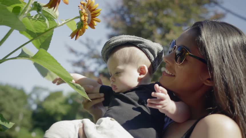 A mother and baby look at flowers outside on a sunny day