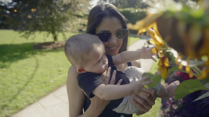 A woman holds a baby up to show him sunflowers in the garden
