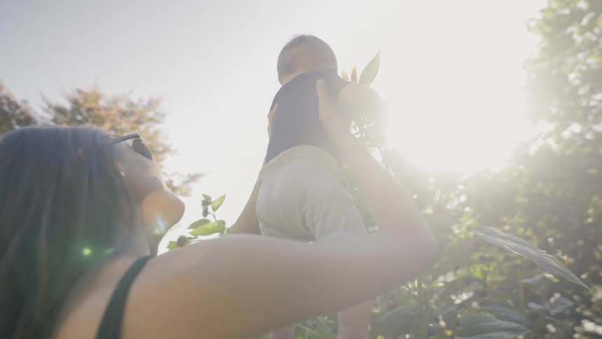 A woman lifts a baby upward to see a tall sunflower