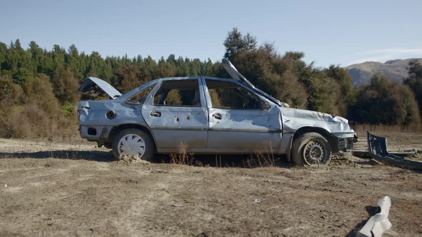 Beat up broken down car sits by dirt road in forest