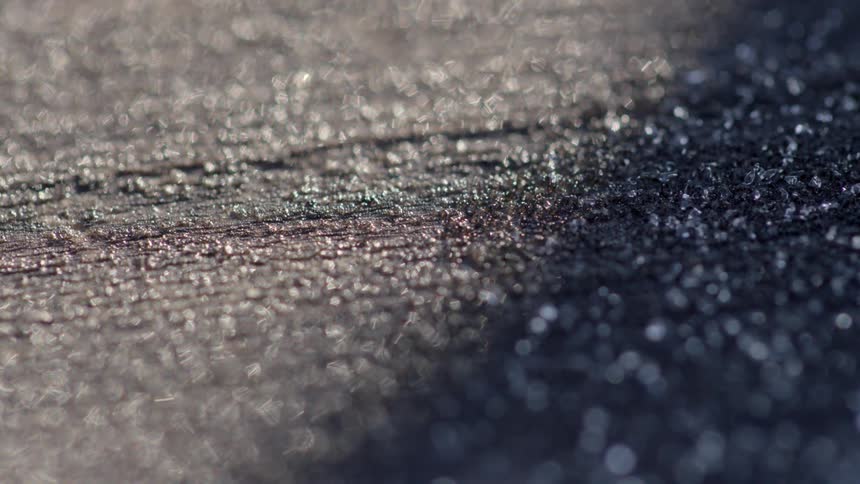 Ice crystals melt on asphalt as the sun shines