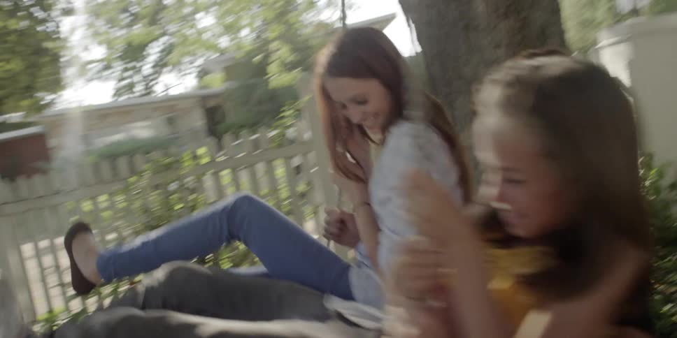 Three youngsters smile as they swing together on a rope swing hung from a tree