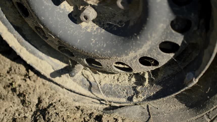 A vehicle tire and rim is partially buried in dirt
