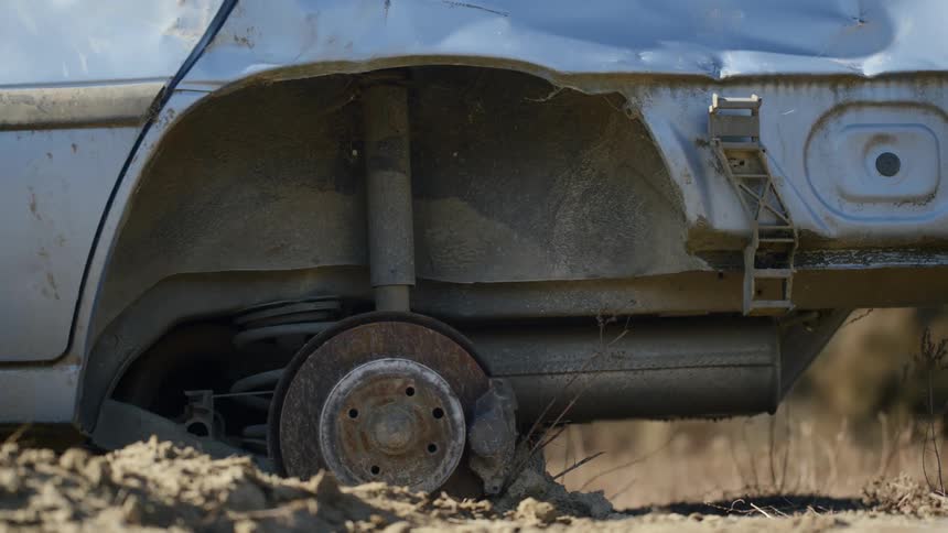 Close up of an abandoned car stripped of its tires in a field