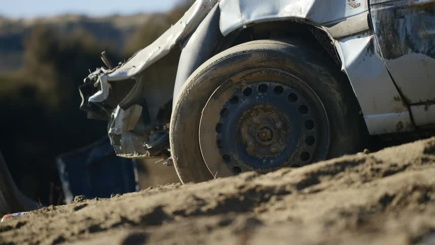 A crashed up car sits in some mud