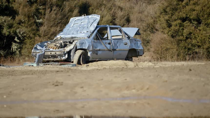 An abandoned stripped car sitting on a dirt road in the mountains