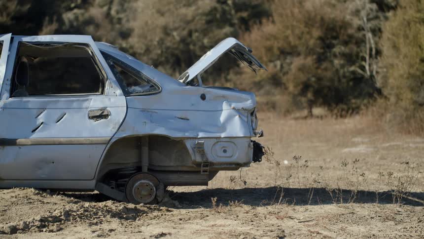 An abandoned car with no tires sits in a dirt field