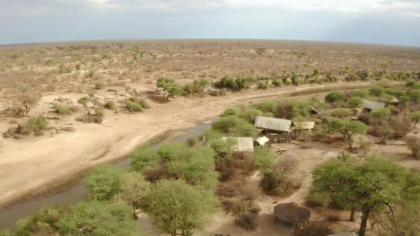 In a wide open arid area a river passes by a remote cluster of buildings constructed amist a grove of trees