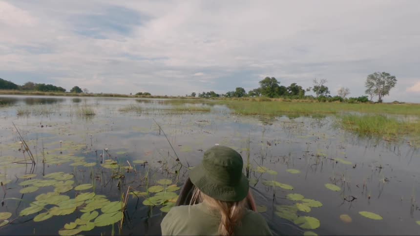 Woman wearing hat rides canoe through marsh at day