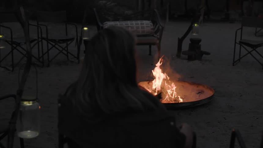 A woman is sitting near a campfire