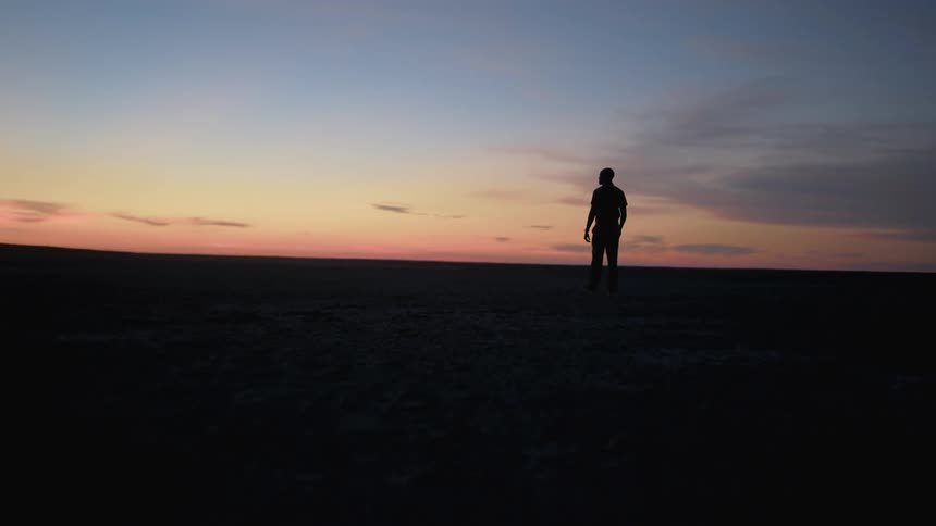 Mans silhouette walks across the field at dusk