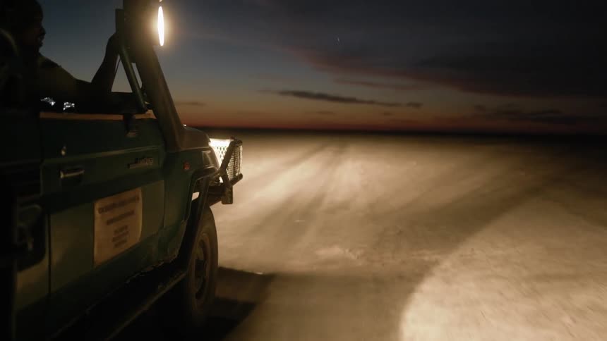 A vehicle traveling through a barren landscape at night