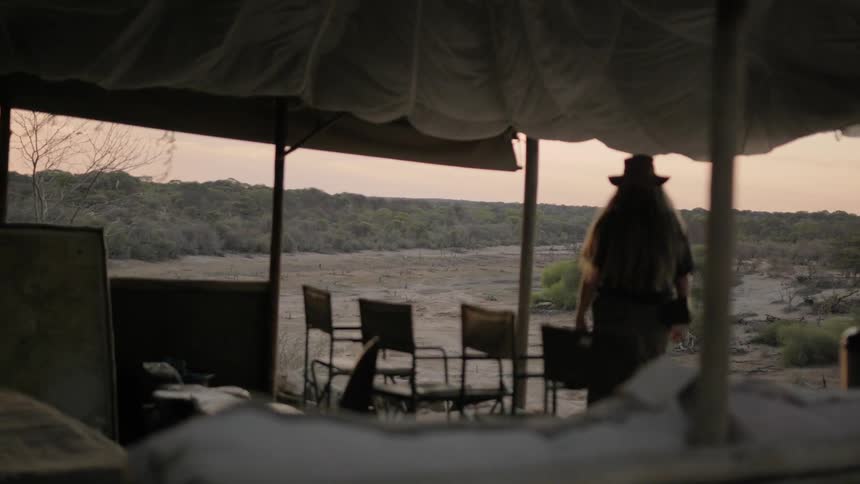 Woman in hat and long skirt walks in front of cabana in desert