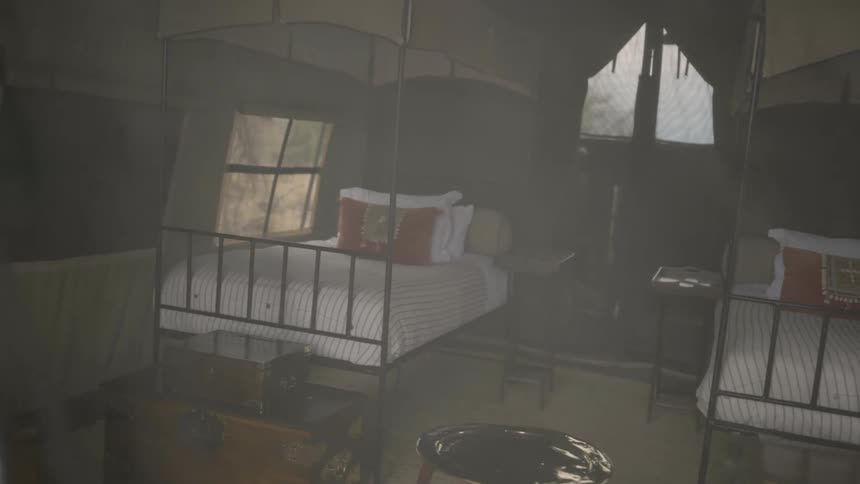 Two beds with canopies set up in a large tent with furniture and rugs