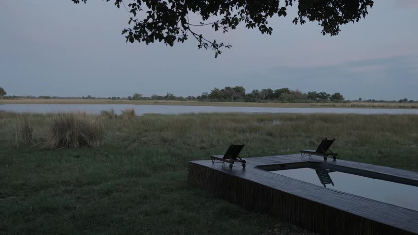 An outdoor pool with two deck chairs is near to a calm river