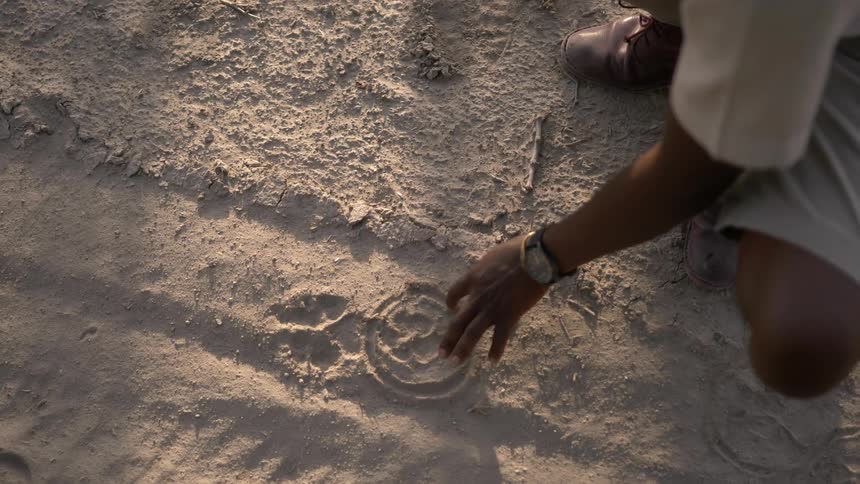 A black man uses his finger to draw in the sand
