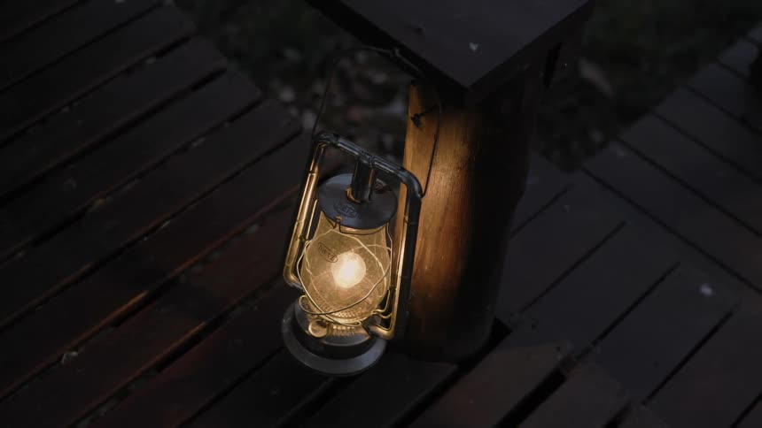 A single lantern sits on a step atop an outdoor wooden deck and next to a support post