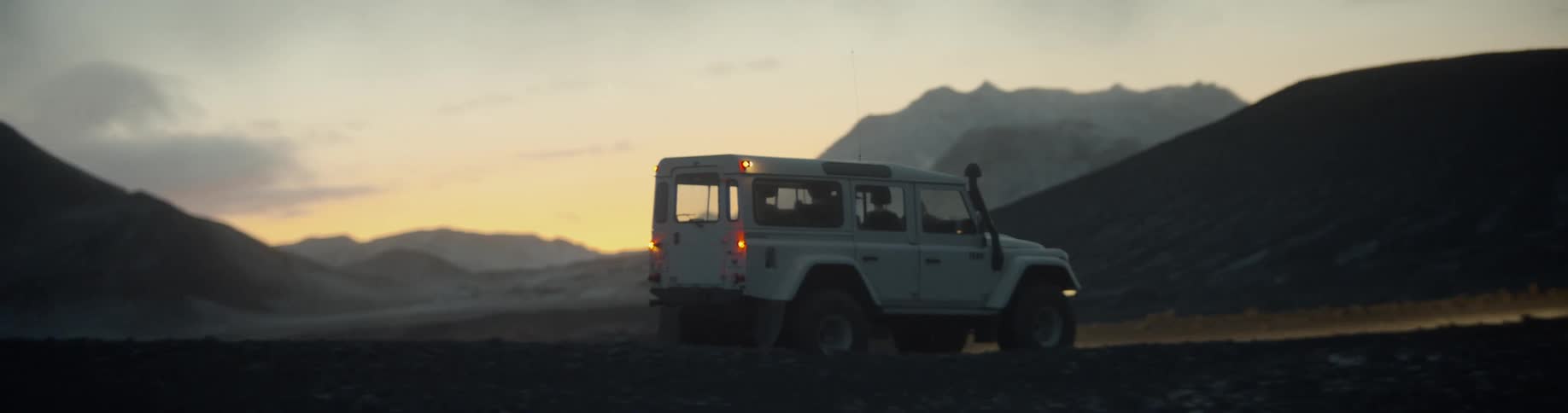 A sport utility vehicle drives through the desert as the sun sets